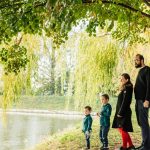 A family enjoys a peaceful walk by a lakeside under a willow tree during autumn.