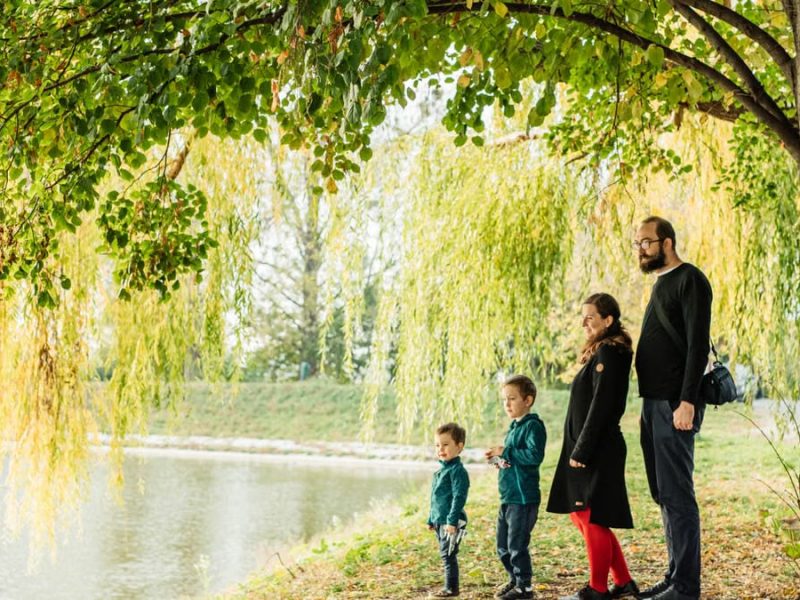 A family enjoys a peaceful walk by a lakeside under a willow tree during autumn.