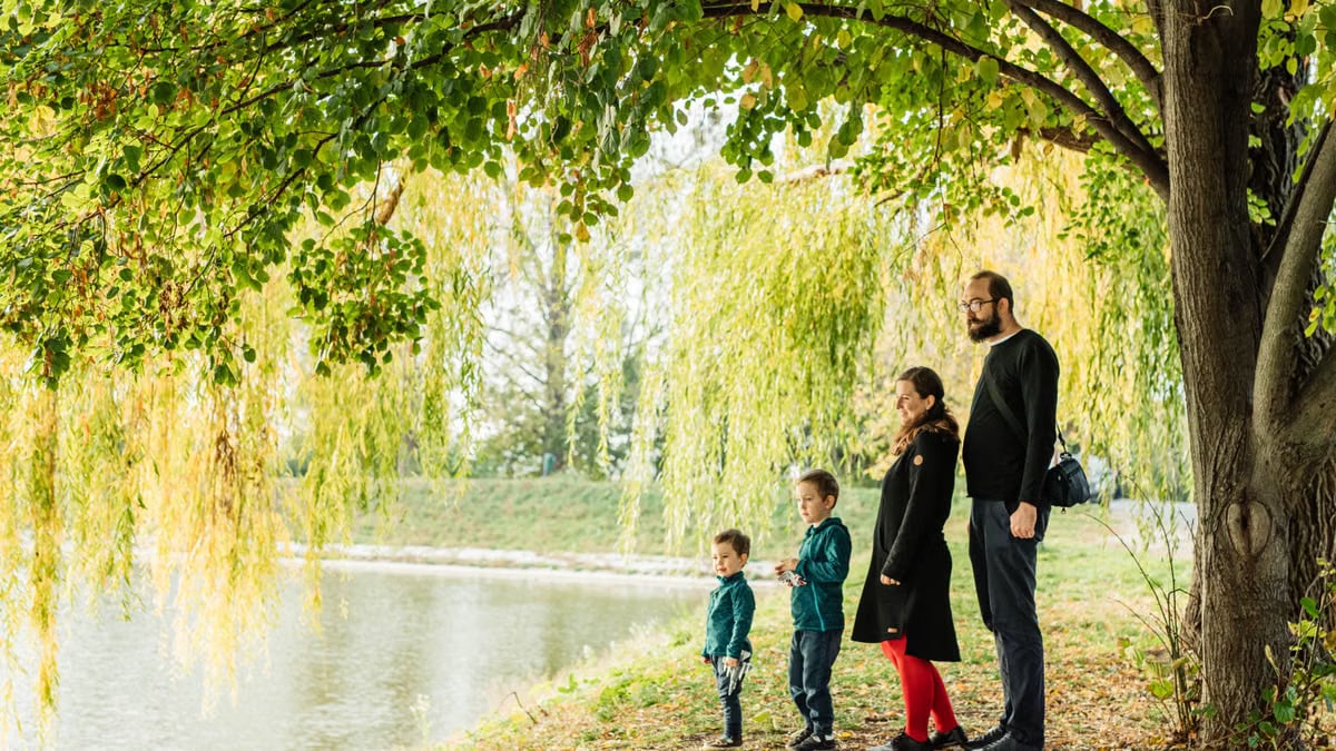A family enjoys a peaceful walk by a lakeside under a willow tree during autumn.